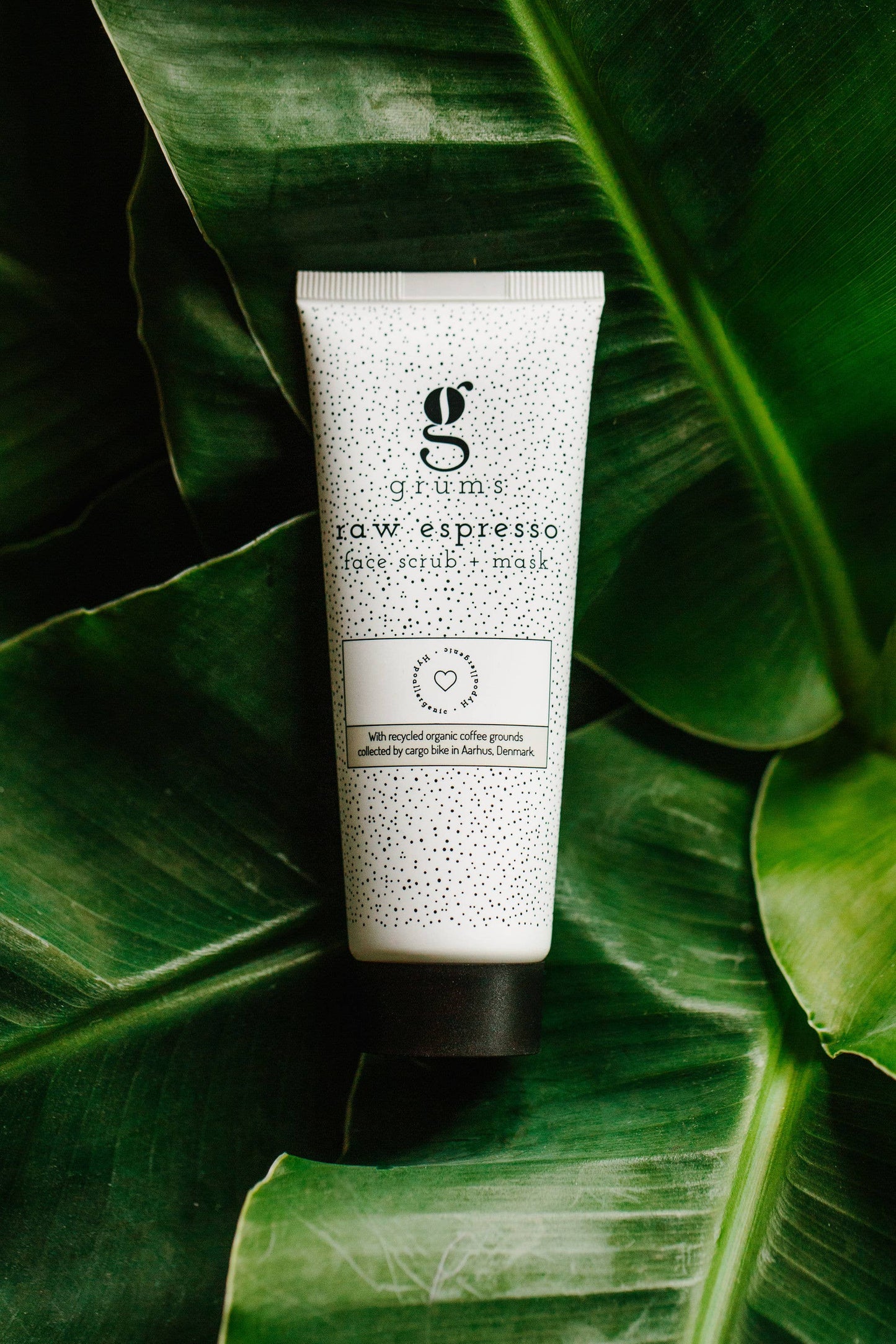 grums Raw Espresso Face Scrub + Mask Tube auf grünen Blättern. Nachhaltige Hautpflege mit natürlichen Inhaltsstoffen.