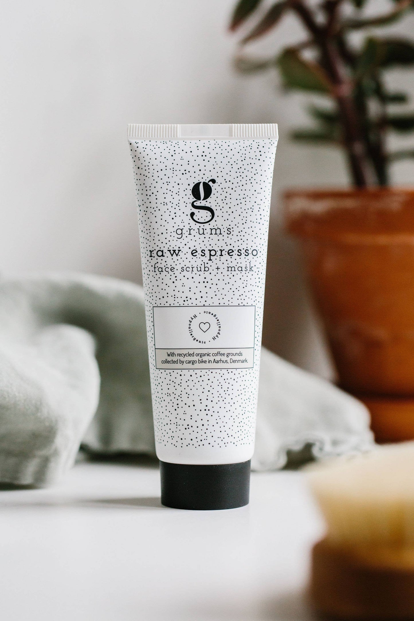 grums Raw Espresso Face Scrub + Mask Tube auf Badablage mit Pflanzen im Hintergrund. Nachhaltige Hautpflege aus Dänemark.