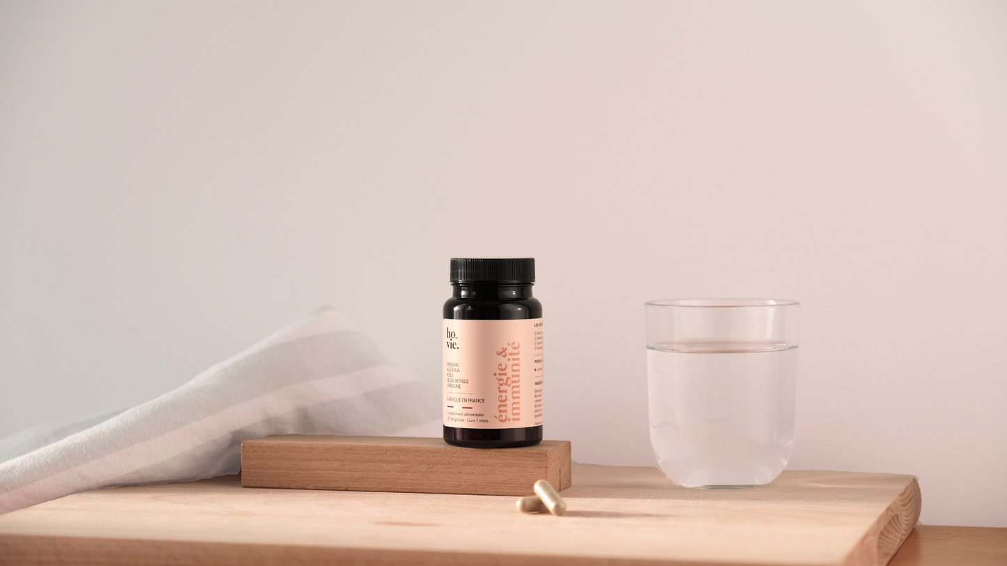 hovie Énergie & Immunité Dose auf Holzunterlage neben einem Glas Wasser und Kapseln.