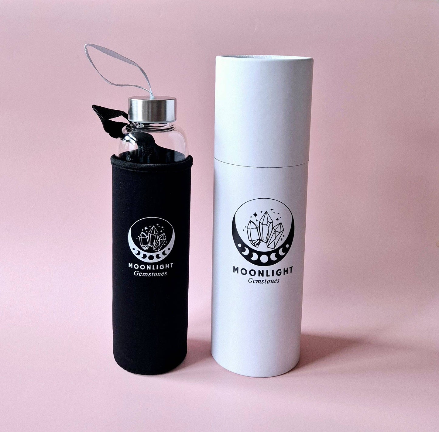 Moonlight Crystal Glas-Trinkflasche mit weißer Geschenkverpackung und schwarzer Schutzhülle vor rosa Hintergrund.