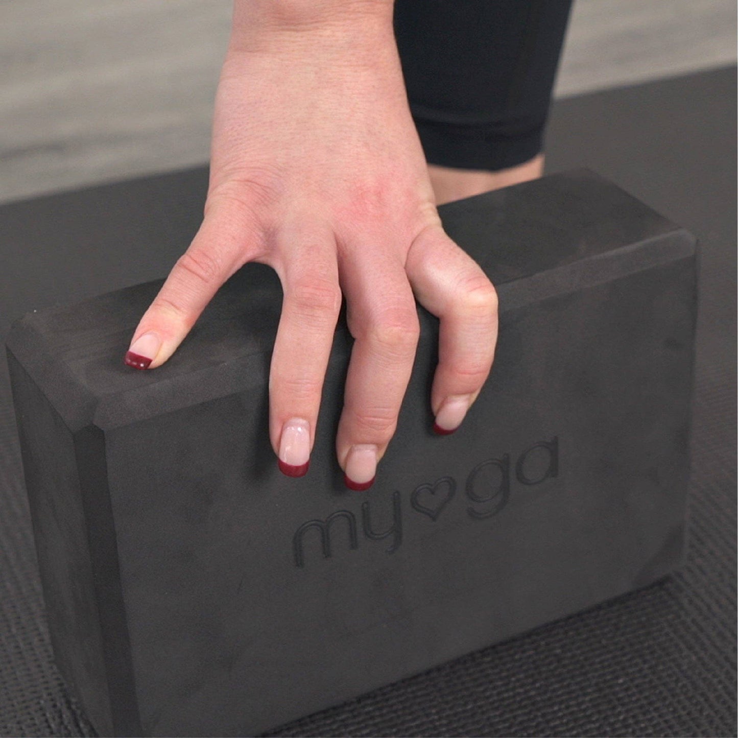 Nahaufnahme einer Hand, die einen schwarzen Myga Yogablock greift. Zeigt ergonomische Form und rutschfeste Oberfläche des Blocks.