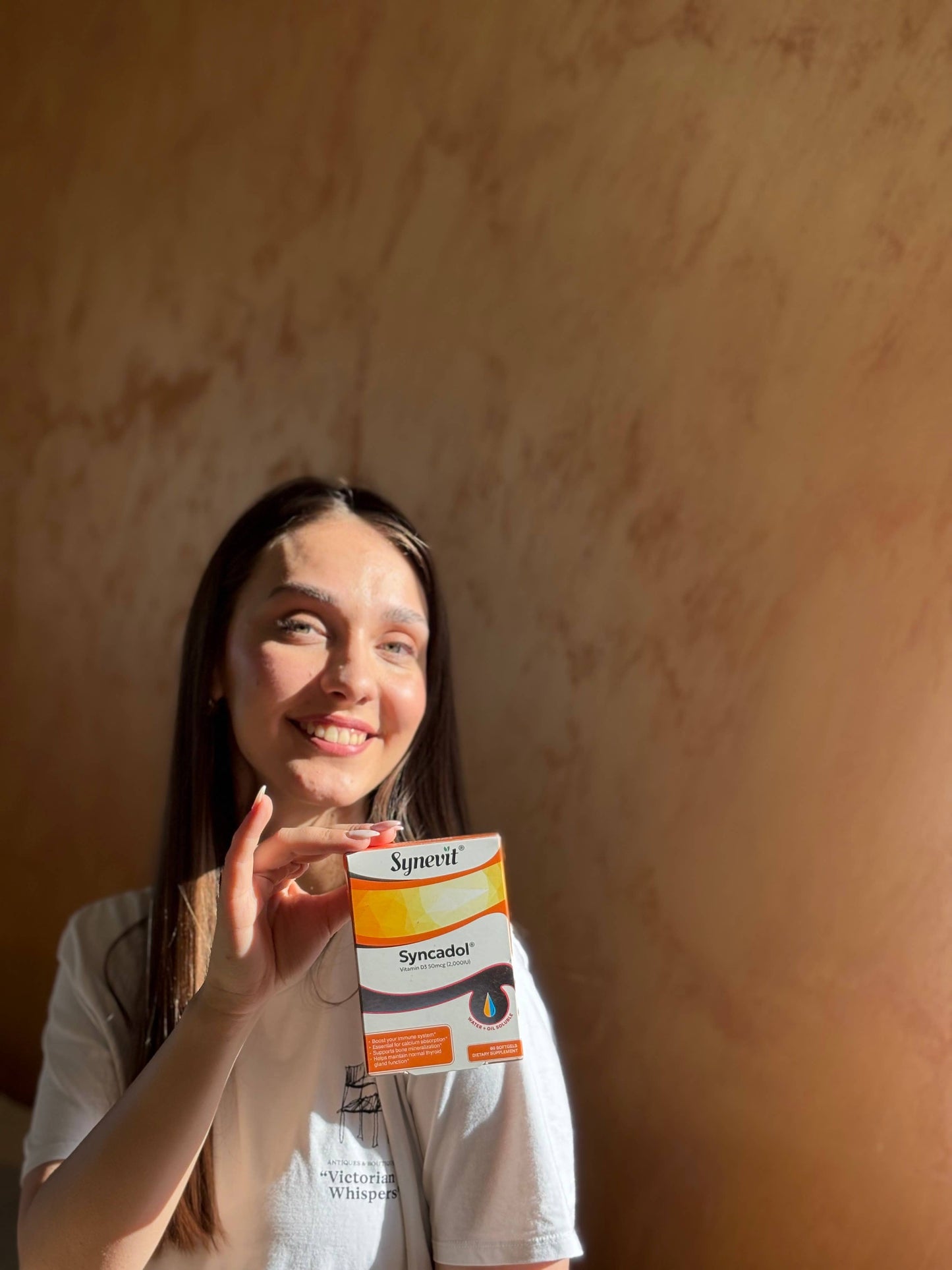 Frau hält eine Packung Synevit Syncadol Vitamin D3 natürliche Aufnahme mit Sonnenlicht.