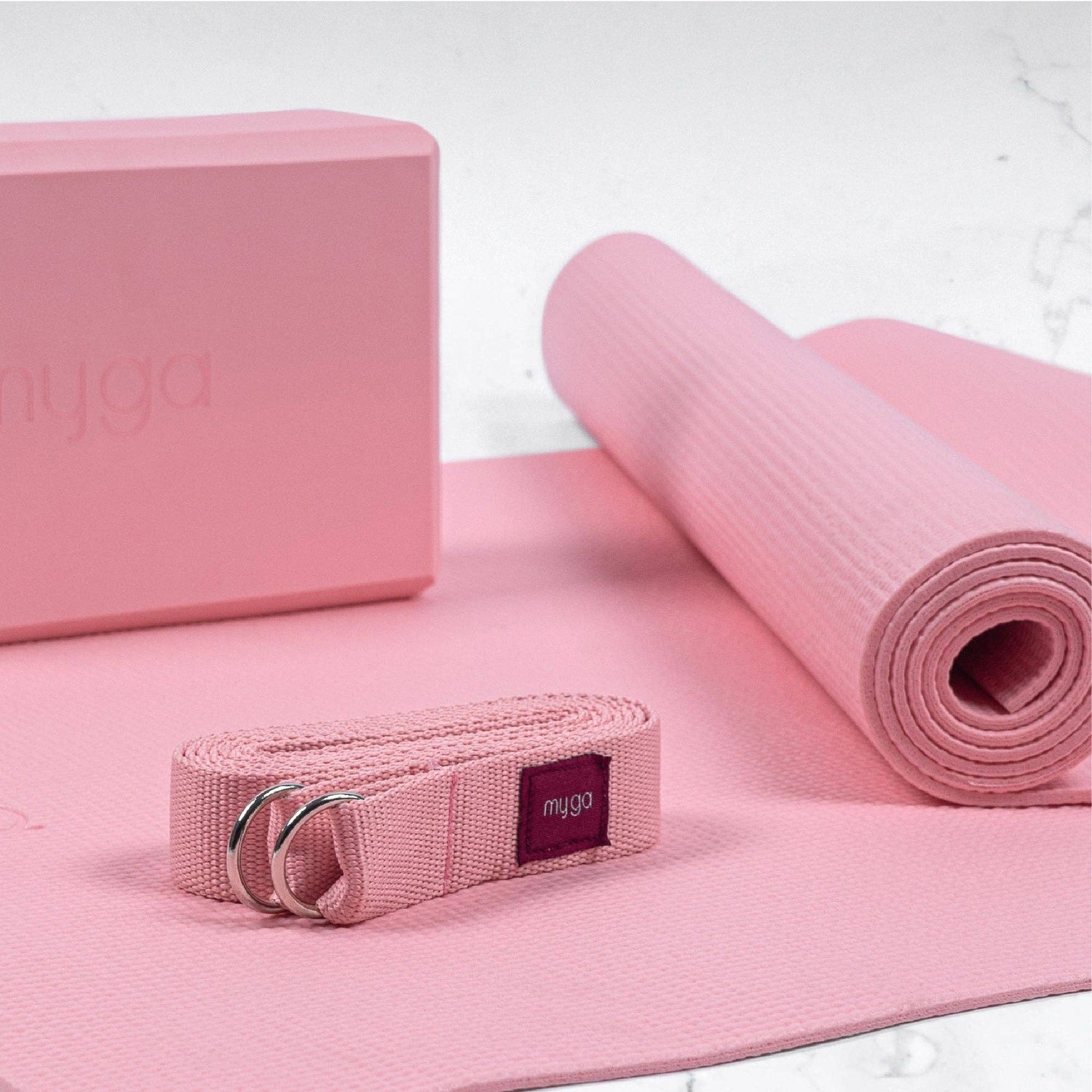 Rosa Yoga-Set bestehend aus Yogamatte, Yogablock, Yogagurt und aufgerollter Matte der Marke Myga