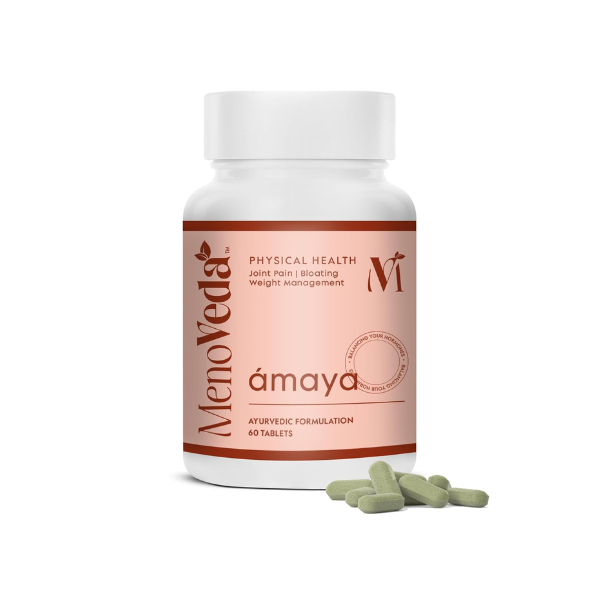 Weiße Kunststoffdose mit rosafarbenem Etikett der Marke MenoVeda, Produktname Amaya. Die Dose enthält 60 ayurvedische Tabletten. Vor der Packung liegen mehrere grüne Tabletten