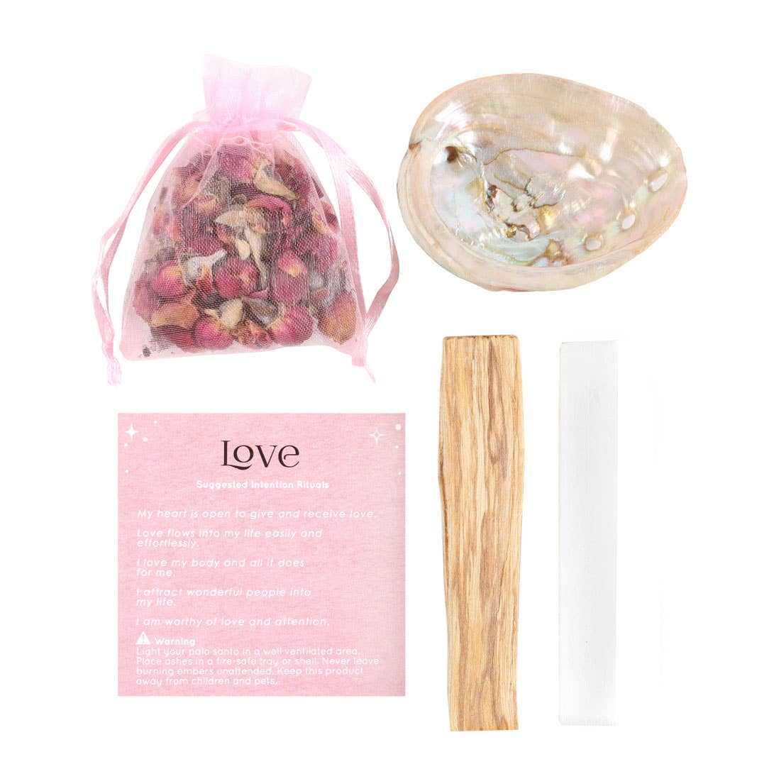 Set aus spirituellen Ritual-Artikeln rosa Organzabeutel mit Rosenblüten, Muschel-Schale, Holzstück, weißer Kristallstab und rosa Karte mit Aufschrift Love