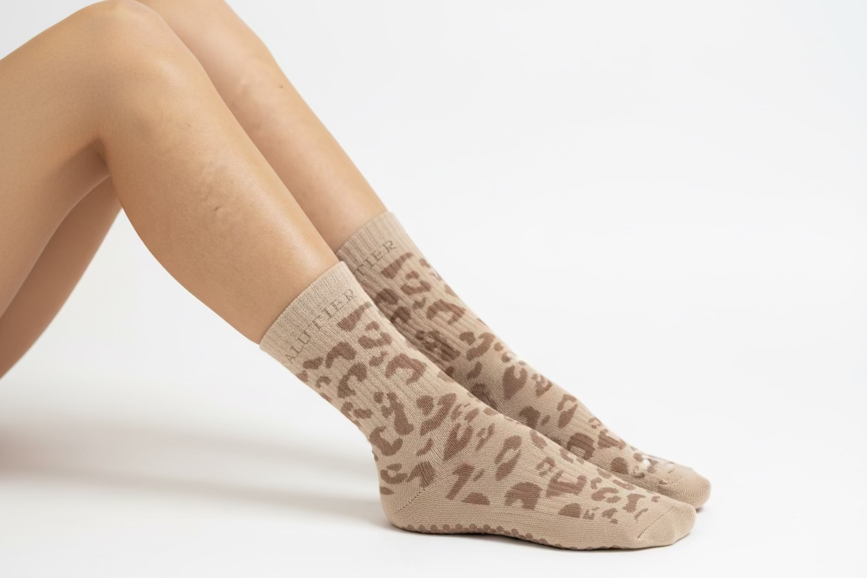 Eine Frau sitzt auf dem Boden mit Pilates Socken. Es sind nur die Beine und Füße zu sehen
