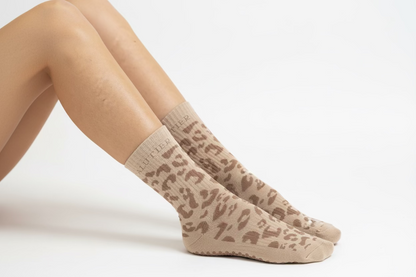 Eine Frau sitzt auf dem Boden mit Pilates Socken. Es sind nur die Beine und Füße zu sehen