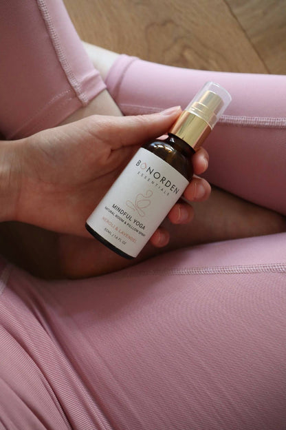 Hand hält eine BONORDEN Mindful Yoga Sprayflasche über rosafarbener Yogahose. Natürliches Raumspray mit Neroli und Lavendel für Ruhe und Achtsamkeit beim Yoga.