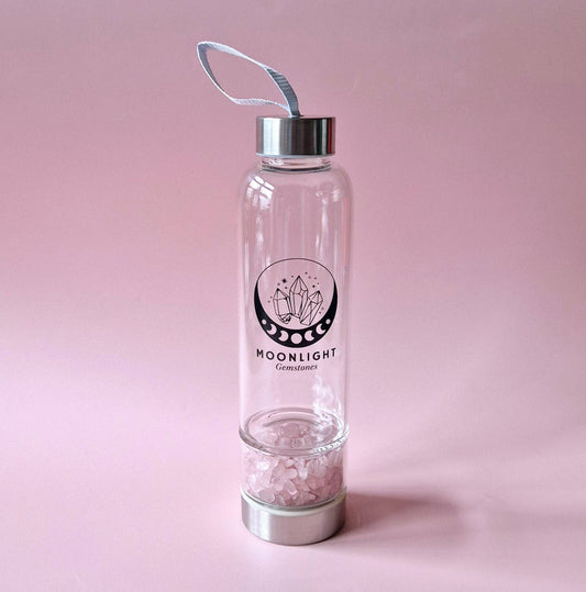 Glas-Trinkflasche Moonlight Crystal mit Edelsteinfach und Silberdeckel vor rosa Hintergrund. Stilvolle Flasche mit Trageschlaufe.