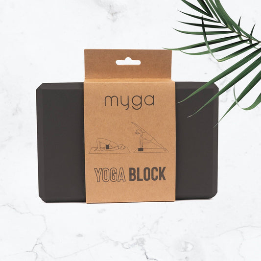 Schwarzer Yogablock von Myga in Verpackung aus braunem Karton auf hellem Hintergrund mit grünen Blättern. Nachhaltiges Yoga-Zubehör für Balance und Unterstützung bei Übungen.