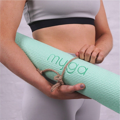 Frau hält zusammengerollte grüne Yogamatte mit Myga-Logo in den Armen. Leichte, tragbare Matte für Yoga und Fitness.